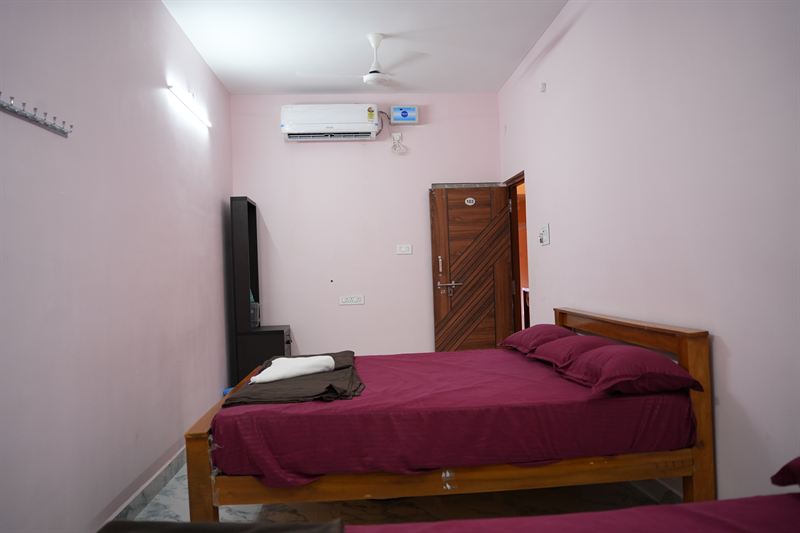 Standard non-AC room with pink walls, wooden bed and dressing area